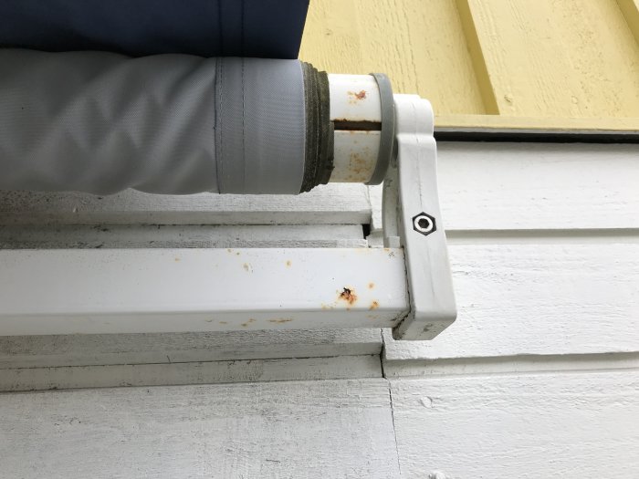 Rörända fast vid en vit vägg med en axel och en avtagbar vevklump till vänster, möjligt justeringsbehov.