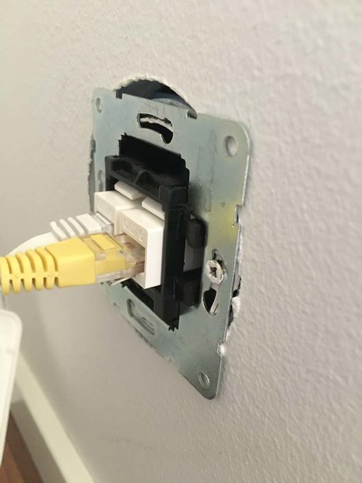 Ett nätverksuttag som sticker ut från väggen med en ansluten gul nätverkskabel.