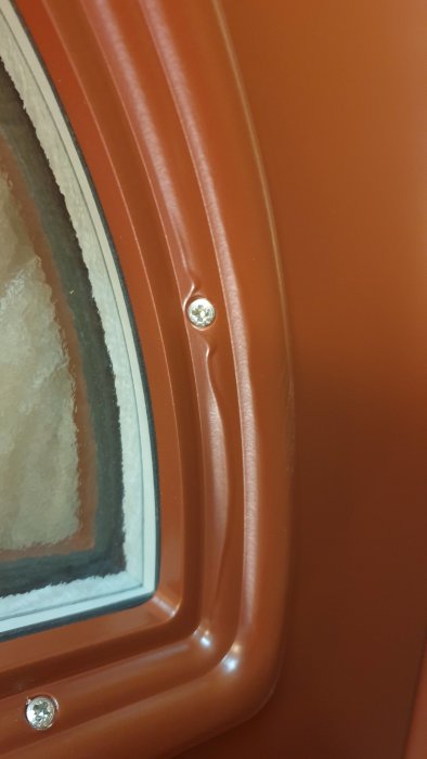 Närbild på orange ytterdörr med färg som runnit ned längs list vid fönsterkant.