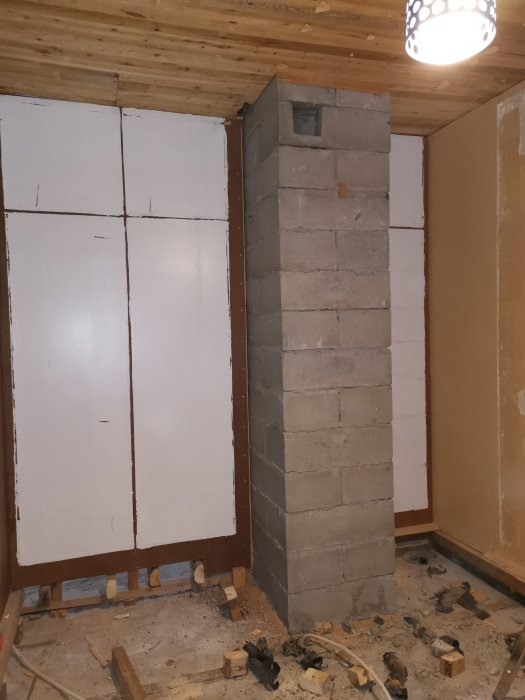 En oavslutad skorsten av betongblock i ett renoveringsprojekt inomhus, med byggavfall på golvet.