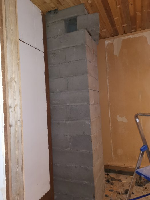 Obyggd skorsten av betongblock i ett renoveringsprojekt med träarbeten och stege i bakgrunden.