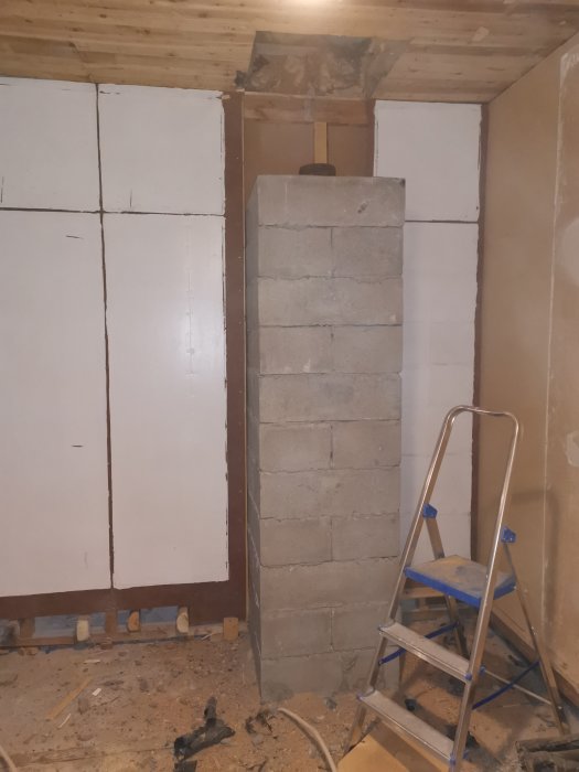 Betongblock staplade till en pelare vid en vägg under renovering, med en stege bredvid.