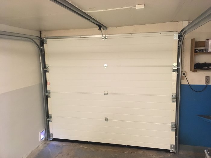 Nyinstallerad vit sektionsgaragedörr stängd, synliga gångjärn och räls, i ett garage.