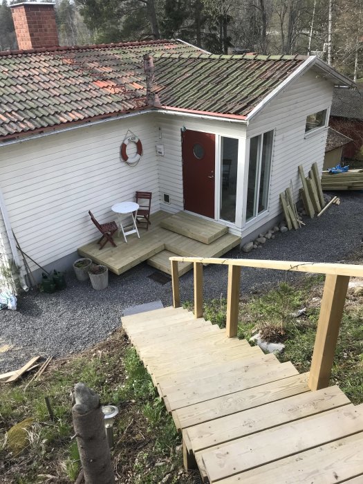 Vy över trädäcket och vita sidan av ett hus med rött tegeltak, en röd dörr och en livboj dekoration.
