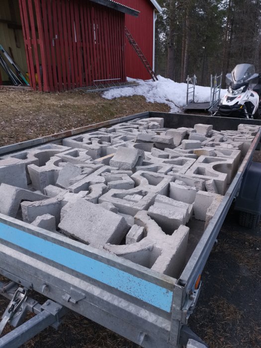 Lastbilssläp fullt med trasiga betongblock från en demonterad skorsten, framför en röd stuga och snö.