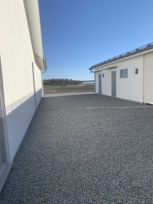 Vitputsad byggnadsfasad i solen med Caparol-fasadputs, grusgång och blå himmel.