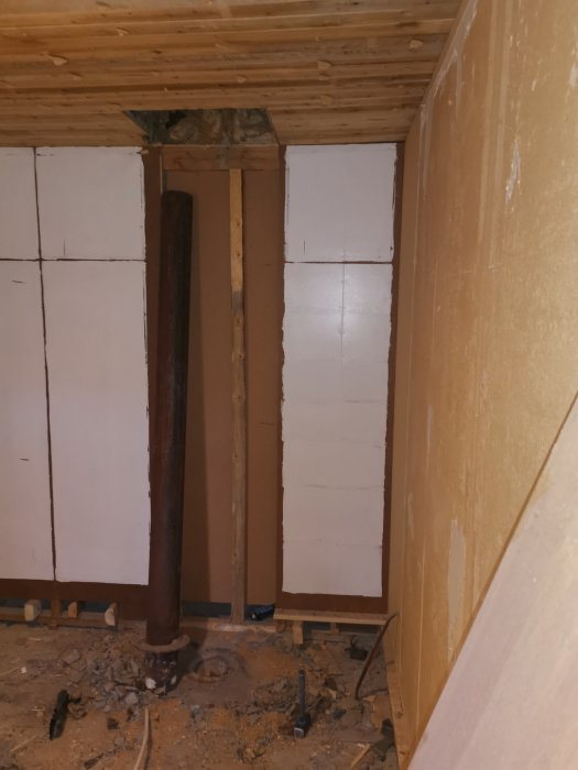 Gammal kraftig rörstolpe mitt i rivningsarbete inomhus med synliga reglar och byggbråte.