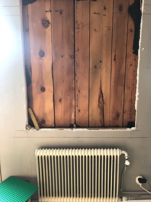 Invändig vy av en vägg före fönsterinstallation, med synlig stomme av stående plank och en radiator framför.