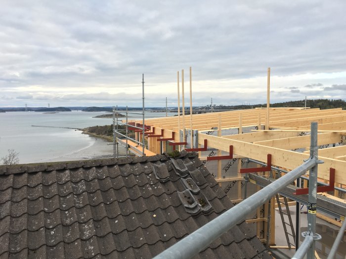 Stomme och tak av en byggnad under konstruktion med utsikt över havet och en stad i bakgrunden.