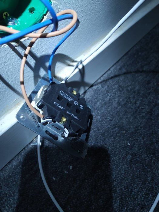 Bild på en elinstallation med öppen strömställare och oskyddade kablar i olika färger.