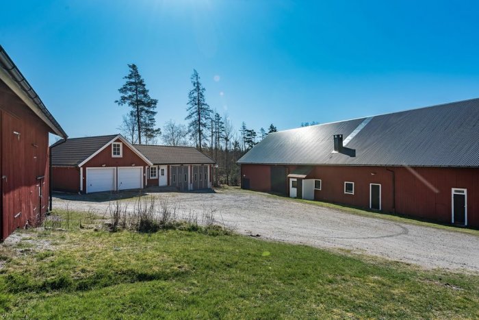 Fastighet med liten bostad mellan ett dubbelt garage och en stor maskinhall omgiven av skog.