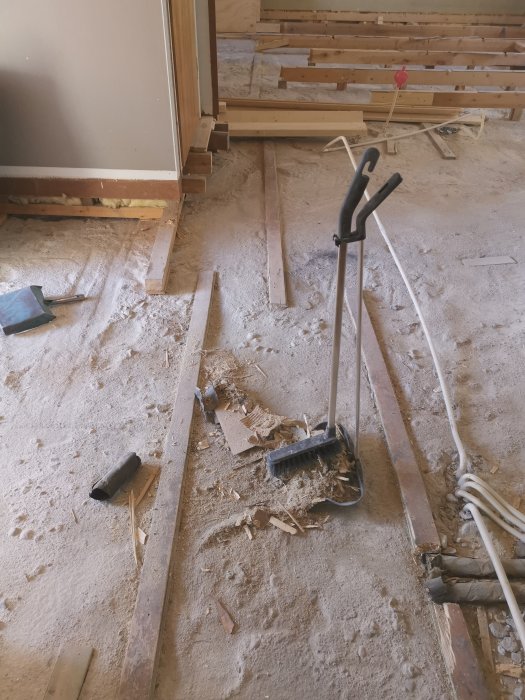 Arbetsplats inomhus med städning under pågående byggprojekt; skräp, spån, verktyg och osorterat byggmaterial på golv.