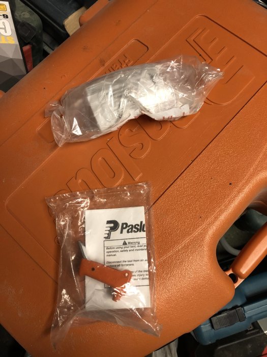 Paslode PSN90 spikpistol i en öppnad orange låda med skyddsglasögon och manual ovanpå.