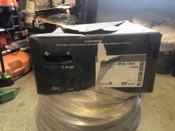 Elkabel i en öppnad PowerLine förpackning, märkt "PNIFK 3G2,5 White 16mm", ligger på ett arbetsbord.