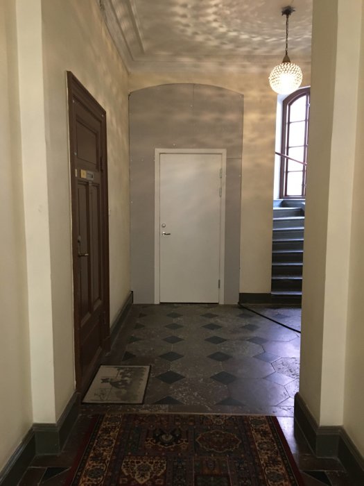 Provisorisk dörr i en trappuppgång med mönstrat golv och trappa i bakgrunden.