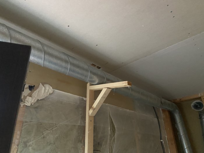 Ventilationsrör som går genom ett orenoverat badrum med synliga isoleringsmaterial och konstruktionselement.