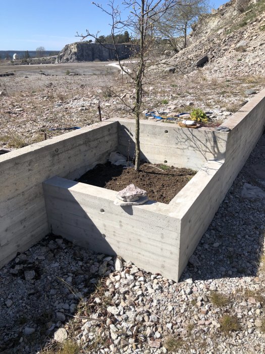 Bild på en L-formad betongmur i olika höjder med grus och natur i bakgrunden.