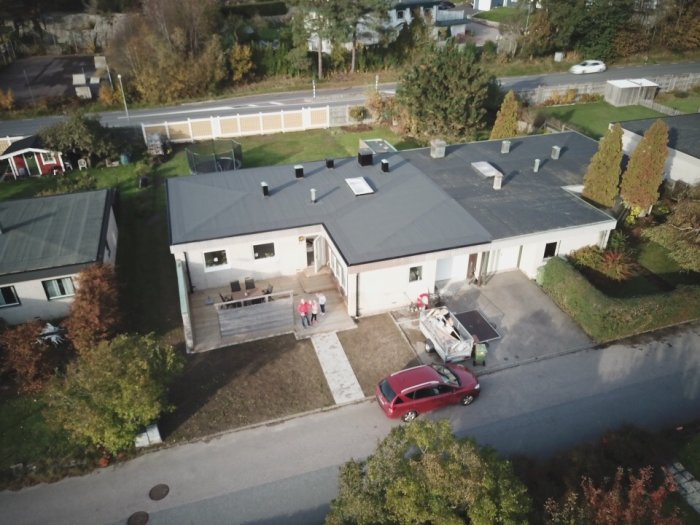 Flygbild av ett grått tvåfamiljshus i mexitegel med bil och personer framför.