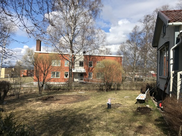 Slänt vid hus med markerad yta för pooldäck, med verktyg och material på gräsmattan.