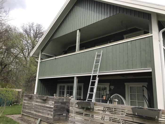 Ny monterad trähandledare på vitt hus med gröna paneler, stege lutad mot balkong, omgiven av byggmaterial.