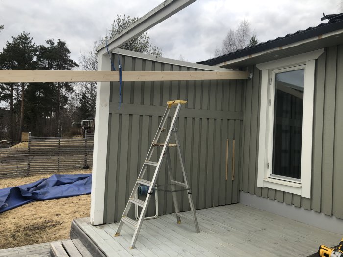 Pågående bygge av skärmtak med synliga takstolar ovanpå uteplats, stegar och verktyg synliga.