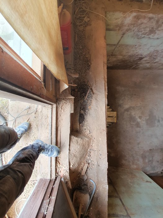 Vy över en öppen jordfylld springa mellan en husvägg och källarvägg under en rivningsfas i ett renoveringsprojekt.