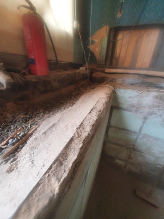 Utsikt över en gammal grund med en synlig jordfylld springa mellan en betongklack och källarväggen i ett rivet bjälklag.