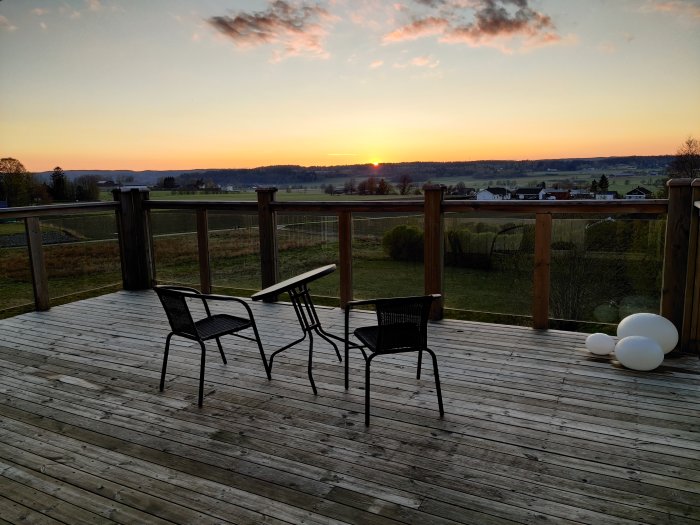 Solnedgång från en träterrass med caféstolar och omkullvält bord, utsikt över landskap.