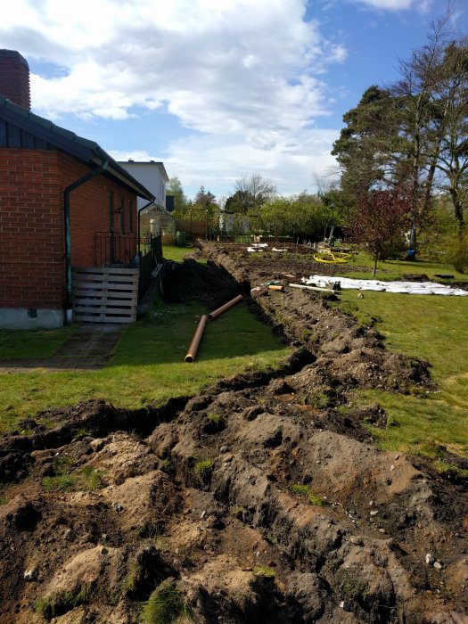 Grävd långsträckt grop i en trädgård med utspridd jord och trädgårdsredskap.