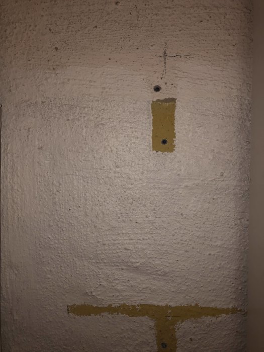 Ojämn källarvägg täckt med vit kalkfärg och delvis synlig gul märkning.
