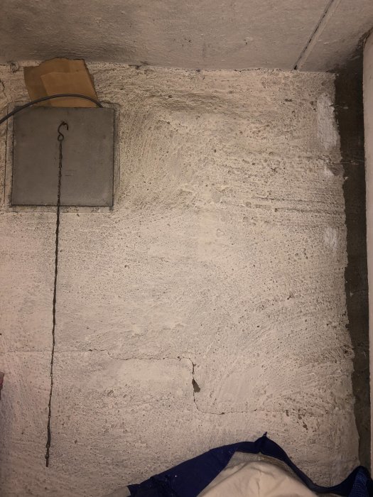 Ojämn källarvägg med vit kalkfärg och synliga oregelbundenheter, med en del sprickor och slitet puts.