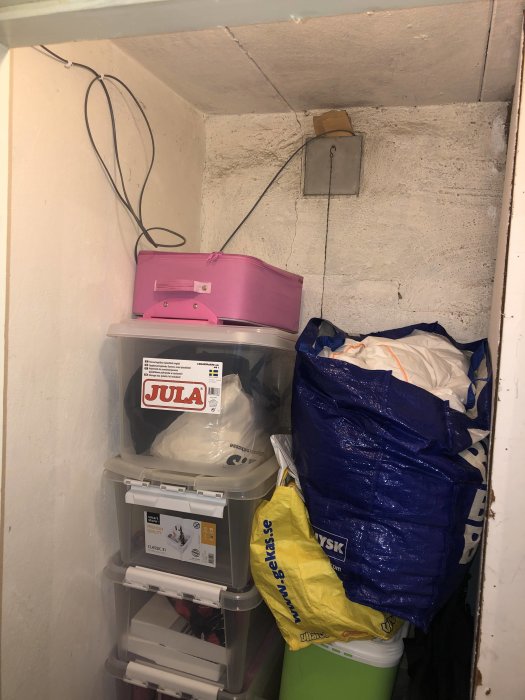 Ojämna kalkfärgade källarväggar med förvaringslådor och blå och gul shoppingkasse.