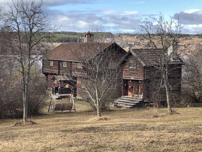 Traditionella röda trähus på Sjövalla gård omgivna av kala träd och en äng i våranda.