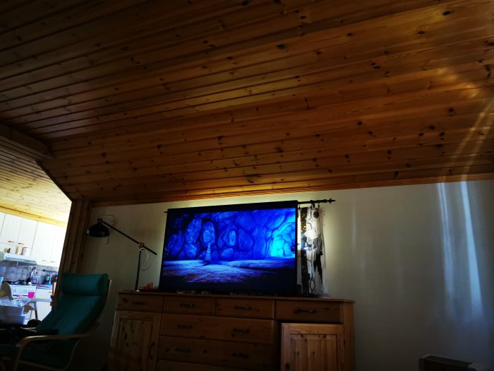 Inredning av ett rum med träpanelstak och en TV på en byrå. Skadad vägg synlig med isoleringen som sticker ut.