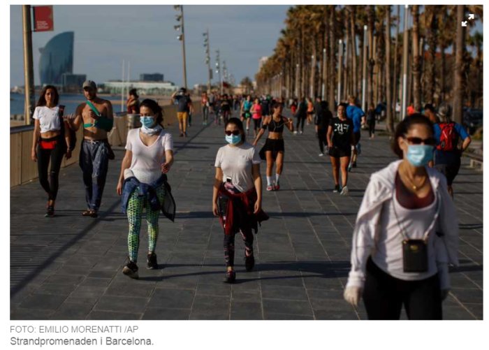 Människor med ansiktsmasker som promenerar på en strandpromenad i Barcelona.