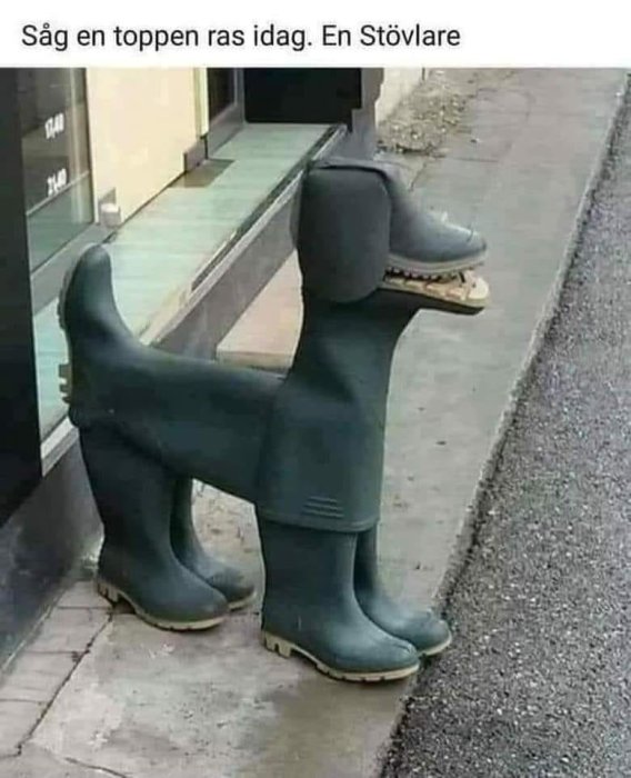 Skulptur föreställande en hund uppbyggd av gröna gummistövlar med en svart huvudform på en trottoar.