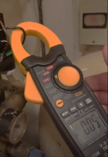 Multimeter som visar 0.05 ampere under mätning, i en något rörig inomhusmiljö.
