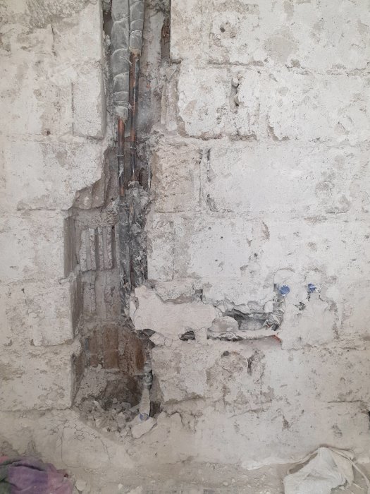 Vägg med avtäckt kanal där vattenrör och hönsnät syns, gamla puts- och kakelrester, i renoveringsprojekt.