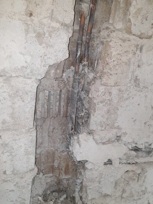 Renoverad källarvägg med exponerade, gamla vattenrör och borttaget kakel, hönsnät och puts.