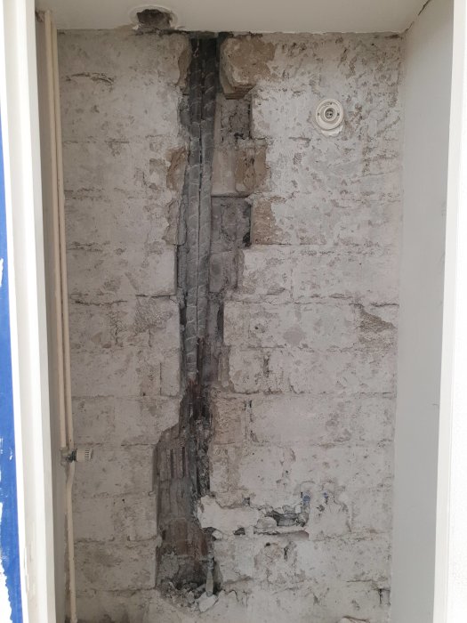 Renoveringsarbete på gästtoalett med synliga vattenrör och hål i väggen efter borttaget kakel.