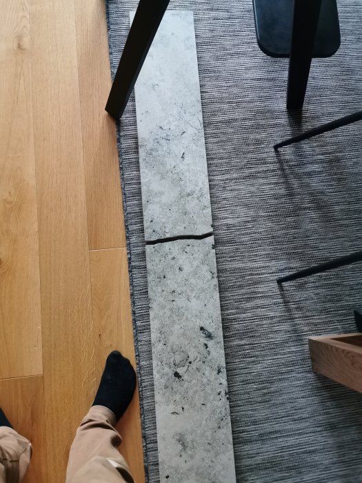 Sprucken fönsterbänk i sten ligger på ett golv med en svart strumpkläd person intill.