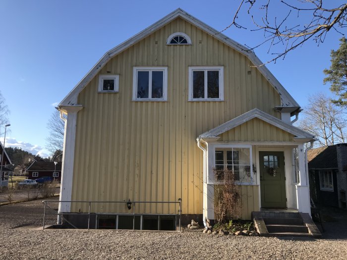 Gult trähus med vita fönster och entré under en klarblå himmel.