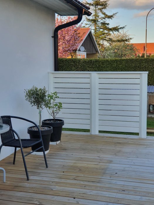 Nybyggd träaltan med vit väggskyddspanel, utemöbler och krukväxter, omgiven av grönska.