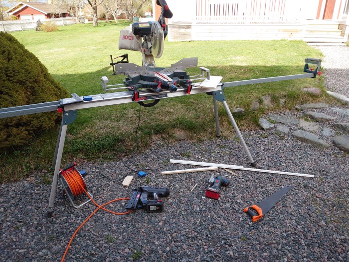 Bosch kapsåg på sågbord med träbitar och verktyg utspridda på en grusdrivbana utomhus.
