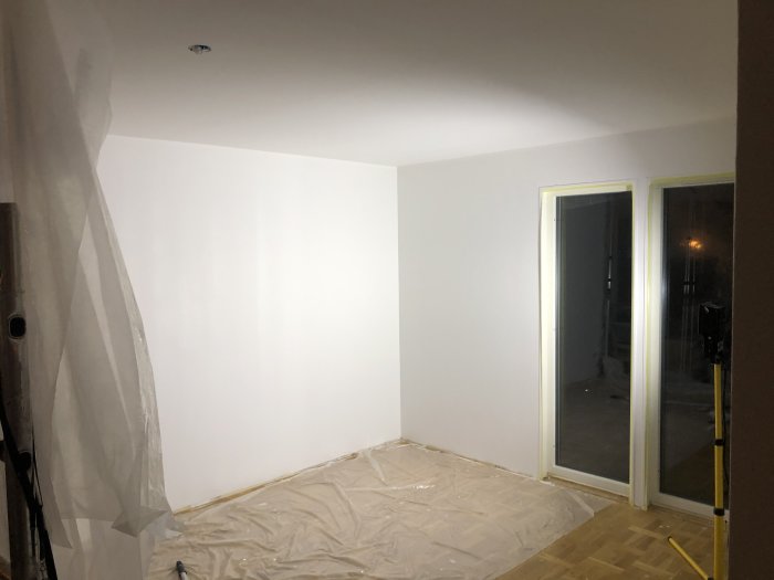 Nyrenoverat rum med nymålade vita väggar och skyddsplast på golvet.