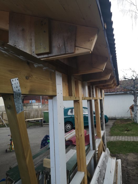 Carport under konstruktion med trästolpar och takstöd, bekymmer över stabiliteten nämns.