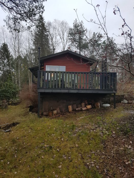 Röd stuga med svart tak och utskjutande veranda i naturen, planer för tillbyggnad diskuteras.