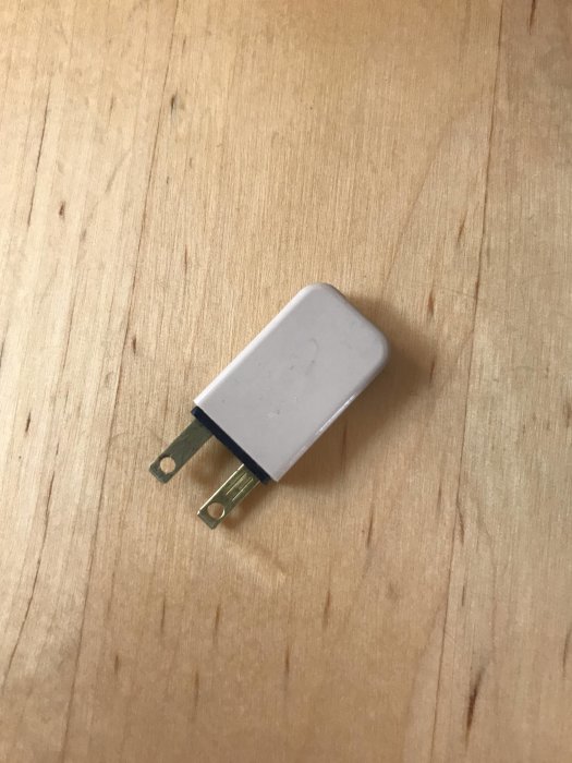 Vit elektronikkomponent med två metallflikar på ett träbord, okänd funktion och utan märkning.