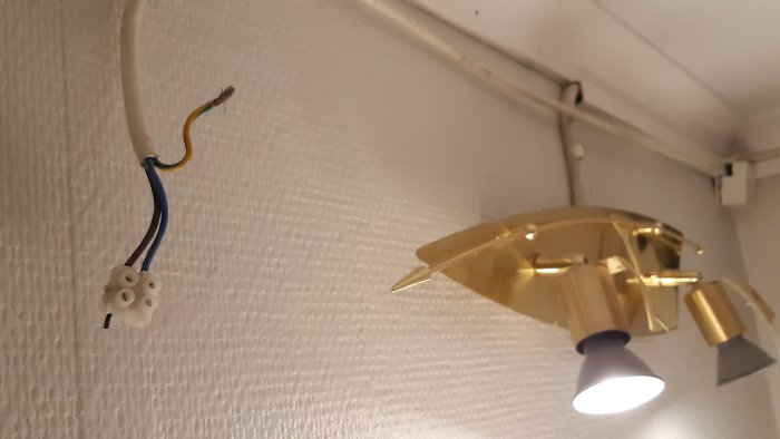 Oslutad elektrisk anslutning och guldtonad lampa med tre ljuskällor på en restaurang i Grebbestad.