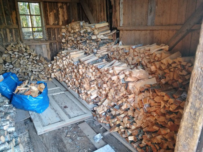 Stapel av nyligen kluven ved i en vedbod med en öppen dörr och ett fönster.